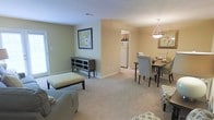 Located at 8 Merry Ln in Greenville, NC, this single-floor residence offers a welcoming and efficiently designed living space. The open-concept layout seamlessly connects the living room and dining area, creating a cohesive and functional floor plan ideal for both everyday living and entertaining.

The living area is finished with soft, wall-to-wall carpeting and painted in warm, neutral tones that lend a calm and inviting atmosphere throughout. Natural light filters into the space, enhancing the brightness of the interior. A dedicated wall space accommodates decorative artwork, adding a personal touch to the room.

The dining area is positioned adjacent to the living room and is outfitted with an elegant pendant light fixture that draws the eye and adds a refined focal point to the space. The dining setup comfortably accommodates multiple guests, making it well-suited for shared meals and gatherings.

A clear sightline from the living and dining areas leads directly into the kitchen, which features standard appliances including a full-size refrigerator, providing convenient access and an open, connected feel between the home's main living zones.

Overall, the space presents a tidy, well-maintained interior with a cohesive color palette, functional layout, and comfortable finishes that make it a practical and pleasant place to call home.