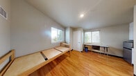 Located at 4730 20th Ave NE in Seattle's University District, this single-floor unit offers an efficient, well-organized layout comprising one bedroom and one bathroom. The main living area features warm hardwood flooring that extends throughout, neutral-toned walls, and windows fitted with blinds that allow natural light to filter in while maintaining privacy. A compact kitchenette is tucked into one corner of the space, equipped with white cabinetry, a microwave, a sink, and a mini-refrigerator — providing essential cooking and storage functionality within a modest footprint. The bedroom area is straightforward and practical, accommodating a twin bed frame and offering enough room for a desk and chair, making it well-suited for focused living or studying. A window in the bedroom looks out toward surrounding greenery, adding a sense of openness. The bathroom is clean and functional, outfitted with a white vanity with under-sink storage, a toilet, a mirrored medicine cabinet, and stainless steel grab bars along the walls, indicating accessibility-conscious design. Light tile flooring and neutral wall tones keep the bathroom bright and easy to maintain. Overall, the unit presents a no-frills, efficient living environment well-positioned for residents seeking proximity to the University of Washington campus.