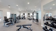 The fitness center is a spacious, single-level facility designed to support a comprehensive workout routine. The room features a clean, modern aesthetic with white walls, crown molding, and a smooth light gray ceiling equipped with recessed lighting that ensures consistent, even illumination throughout the space. Natural light filters in through multiple windows, enhancing the bright and energizing atmosphere.

The facility is outfitted with a variety of Matrix-brand equipment, including cable resistance machines, a multi-function strength training tower, and a weight bench, providing ample options for strength and resistance training. Cardio equipment includes treadmills and an elliptical trainer, positioned to allow comfortable spacing between users. Wall-mounted televisions are strategically placed for viewing during workouts.

The flooring consists of durable, low-pile material suited for fitness use, providing both comfort and easy maintenance. The open floor plan allows for easy navigation between equipment stations. A mirrored wall on one side enhances the sense of space while supporting form checks during exercise. Overall, the fitness center offers a clean, functional, and inviting environment for residents or members.