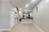 Located at 205 Hawley Ave in Syracuse, NY, this two-story home offers a clean, modern aesthetic with fresh finishes throughout. The main floor features light luxury vinyl plank flooring that flows seamlessly from the open living area into the kitchen. The kitchen is well-appointed with white shaker cabinetry, dark granite-style countertops, a subway tile backsplash, and a full suite of stainless steel appliances including a refrigerator, range, microwave, and dishwasher. A peninsula provides added counter space and a natural divide within the open layout. Recessed lighting brightens the interior, while a side window allows natural light to filter in. A stacked washer and dryer unit is conveniently tucked beneath the staircase, alongside additional storage. The main floor also includes an entry area with a door featuring a glass panel. Upstairs, two bedrooms are finished with plush carpeting and neutral gray walls. The primary bedroom offers a comfortable footprint with a closet, while the second bedroom features crown molding and a window with natural light. The full bathroom is clean and minimal, appointed with a white vanity, tub-shower combination with white subway tile surround, and matte black fixtures and hardware throughout.