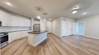 This well-designed 2-bedroom, 2-bathroom residence in Leander, TX offers a thoughtful layout with modern finishes throughout. The kitchen is a standout feature, boasting white shaker cabinetry, dark granite countertops, a subway tile backsplash, stainless steel appliances including a gas range and French door refrigerator, and a central island with globe pendant lighting — ideal for cooking and entertaining. Light wood-style flooring flows through the main living areas, complementing the bright, neutral palette.

Both bathrooms are finished with white vanity cabinetry, dark granite countertops, and large mirrors. One bathroom includes a walk-in marble-tiled shower, while the second features a marble-surround soaking tub and shower combo. The generously sized primary bedroom includes plush carpet, direct access to its en-suite bathroom, and a spacious walk-in closet with built-in shelving and hanging rods. The second bedroom offers comfortable carpeted flooring and clean neutral walls.

A private balcony extends the living space outdoors, offering views of the landscaped community grounds, pool area, and open green space. The exterior presents a clean, contemporary aesthetic with crisp white finishes and modern architectural lines.