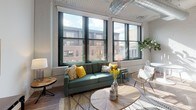 Located at 247 4th St E in the heart of downtown Saint Paul, Minnesota, this single-floor urban loft combines industrial character with modern finishes. The open-concept living area makes a strong impression with soaring ceilings, exposed metal ductwork, and warm hardwood flooring. A bank of large, black-framed windows floods the space with natural light and frames views of the surrounding cityscape, creating a dynamic urban backdrop.

The kitchen is well-appointed with crisp white cabinetry, a herringbone tile backsplash, quartz countertops, and a full suite of stainless steel appliances including a French door refrigerator, electric range with over-the-range microwave, and dishwasher. Painted white brick walls add texture and a nod to the building's historic bones throughout the space.

The bedroom offers a quieter retreat, featuring plush carpeting, a high clerestory window that draws in light, exposed ductwork overhead, and painted brick walls that carry the loft's industrial aesthetic. A pendant light fixture adds an industrial-chic touch to the room.

The bathroom includes a full tub-shower combination with chrome fixtures and clean white surroundings. Overall, the space delivers a compelling blend of historic industrial architecture and contemporary updates in a prime downtown location.