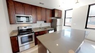 This thoughtfully designed 1-bedroom, 1-bathroom residence spans a comfortable single floor, offering a functional and modern open-concept layout. The living and dining area features large-format light tile flooring, neutral toned walls, and an abundance of natural light streaming through oversized black-framed windows that frame views of the surrounding cityscape.

The kitchen is a standout feature, showcasing rich dark mahogany cabinetry extending to the ceiling for ample storage, complemented by sleek quartz countertops in a warm taupe finish. A generous center island provides additional prep and seating space, while stainless steel appliances — including a range, microwave, dishwasher, and refrigerator — complete the polished look. Stylish pendant lighting hangs above the island, adding a refined touch to the space.

The bedroom is a quiet retreat, carpeted for comfort, with soft neutral walls and a ceiling light fixture. The full bathroom is elegantly appointed with a frameless glass walk-in shower, tile surround, hexagonal mosaic floor accents, and an undermount sink with a clean vanity. A built-in closet with shelving is conveniently located just off the bathroom, offering practical storage solutions. The overall ambiance is clean, contemporary, and move-in ready.