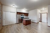 Located at 130 South Olympic Avenue in Arlington, Washington, this well-designed single-floor unit offers a thoughtfully arranged open-concept layout that combines the kitchen, dining, and living areas into one cohesive space. Light-toned luxury vinyl plank flooring runs throughout, providing a clean and consistent aesthetic that ties the rooms together.

The kitchen is a standout feature, equipped with rich dark-wood cabinetry, stainless steel appliances including a refrigerator, range, microwave, and dishwasher, as well as a granite-accented countertop. A central kitchen island adds additional prep and dining space, making it both functional and visually appealing. The living area is distinguished by a full exposed brick accent wall, which lends warmth and character to the space, along with a window that brings in natural light and outdoor views.

Two closets provide practical storage solutions, one of which is a spacious sliding-door closet conveniently positioned near the main living area. The combined bathroom and laundry room offers a well-appointed vanity with dark wood cabinetry, a full-length mirror, and a stacked washer/dryer unit, maximizing the utility of the space. A dedicated entrance completes the layout, ensuring a clear and organized flow throughout the unit.