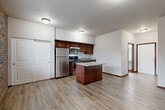 Located at 130 South Olympic Avenue in Arlington, Washington, this well-designed single-floor unit offers a thoughtfully arranged open-concept layout that combines the kitchen, dining, and living areas into one cohesive space. Light-toned luxury vinyl plank flooring runs throughout, providing a clean and consistent aesthetic that ties the rooms together.

The kitchen is a standout feature, equipped with rich dark-wood cabinetry, stainless steel appliances including a refrigerator, range, microwave, and dishwasher, as well as a granite-accented countertop. A central kitchen island adds additional prep and dining space, making it both functional and visually appealing. The living area is distinguished by a full exposed brick accent wall, which lends warmth and character to the space, along with a window that brings in natural light and outdoor views.

Two closets provide practical storage solutions, one of which is a spacious sliding-door closet conveniently positioned near the main living area. The combined bathroom and laundry room offers a well-appointed vanity with dark wood cabinetry, a full-length mirror, and a stacked washer/dryer unit, maximizing the utility of the space. A dedicated entrance completes the layout, ensuring a clear and organized flow throughout the unit.