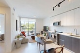 Located at 20775 NW 17th Ave in Miami Gardens, Florida, this thoughtfully designed one-bedroom unit delivers a modern living experience through a clean, open-concept floor plan. The living, dining, and kitchen areas flow seamlessly together, bathed in natural light streaming through floor-to-ceiling sliding glass doors that open onto a private balcony with lush outdoor views. The kitchen is a standout feature, outfitted with two-tone cabinetry — high-gloss white upper cabinets paired with wood-grain lower cabinets — white subway tile backsplash, light quartz countertops, and a full suite of stainless steel appliances including a side-by-side refrigerator, range, microwave, and dishwasher. Track lighting adds a contemporary accent overhead. The living area is bright and airy, with neutral walls and light flooring that carry throughout the unit. The bedroom is a calm retreat with large windows framing outdoor greenery, botanical wall art, and direct access to in-unit stacked laundry — a highly practical feature. The bathroom is finished with a dark wood vanity, white countertop, large mirror, and a tub-shower combination. The overall aesthetic is clean, contemporary, and cohesive throughout.