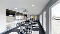 This single-floor fitness center is thoughtfully designed to provide a comprehensive workout environment. The space is anchored by a striking black-and-white graphic accent wall featuring wellness and fitness-themed typography, including prominent words such as "WELLNESS," "GYM," "MUSCLES," and "ATHLETIC," creating an energizing and motivational atmosphere.

The cardio zone is well-appointed with a row of treadmills and stationary cycling bikes, offering ample options for aerobic training. Toward the rear of the space, a cable and strength training station provides additional functionality for resistance-based workouts. A selection of kettlebells and free weights are also available, rounding out the training options.

The facility benefits from a generous bank of windows along one side, flooding the interior with natural light and creating an open, airy feel. Overhead, a combination of recessed lighting and a decorative chandelier-style fixture ensures even illumination throughout. The dark rubberized flooring provides both safety and durability underfoot, while the light gray walls and white ceiling contribute to a clean, modern aesthetic. A ceiling fan toward the rear of the space supports ventilation and comfort during workouts. Overall, the space is designed to be both functional and visually inviting.
