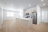 This single-story, 3-bedroom, 2-bathroom home in Idaho Falls, Idaho offers a clean, modern aesthetic throughout. The open-concept kitchen serves as the heart of the home, featuring a large center island with a built-in sink and white quartz countertop, light wood cabinetry with matte black hardware, stainless steel appliances including a refrigerator, electric range, and microwave, and recessed lighting overhead. Light wood-tone luxury vinyl flooring flows seamlessly through the main living and kitchen areas, creating a bright and cohesive feel. The primary bedroom is a comfortable, well-proportioned room, and the primary bathroom includes a wood-tone vanity with white countertop, a tub/shower combination, and a built-in shelving closet. The second bathroom mirrors the modern design with matching cabinetry and fixtures. The two additional bedrooms feature plush carpeting and windows that bring in natural light. A dedicated laundry room houses a full-size top-load washer and dryer. Throughout the home, two-panel white interior doors with matte black hardware add a consistent, contemporary touch. A private patio extends the living space outdoors, rounding out this well-appointed residence.