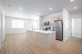 This single-story, 3-bedroom, 2-bathroom home in Idaho Falls, Idaho offers a clean, modern aesthetic throughout. The open-concept kitchen serves as the heart of the home, featuring a large center island with a built-in sink and white quartz countertop, light wood cabinetry with matte black hardware, stainless steel appliances including a refrigerator, electric range, and microwave, and recessed lighting overhead. Light wood-tone luxury vinyl flooring flows seamlessly through the main living and kitchen areas, creating a bright and cohesive feel. The primary bedroom is a comfortable, well-proportioned room, and the primary bathroom includes a wood-tone vanity with white countertop, a tub/shower combination, and a built-in shelving closet. The second bathroom mirrors the modern design with matching cabinetry and fixtures. The two additional bedrooms feature plush carpeting and windows that bring in natural light. A dedicated laundry room houses a full-size top-load washer and dryer. Throughout the home, two-panel white interior doors with matte black hardware add a consistent, contemporary touch. A private patio extends the living space outdoors, rounding out this well-appointed residence.