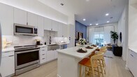 This well-appointed 2-bedroom, 1-bathroom residence offers a cohesive modern design highlighted by light hardwood flooring, recessed lighting, and a clean, neutral palette throughout. The open-concept kitchen is a standout feature, boasting floor-to-ceiling white cabinetry, a large quartz waterfall island with bar seating, stainless steel appliances, a farmhouse sink with a matte black faucet, and a classic tile backsplash. Built-in shelving with LED accent lighting adds both functionality and visual interest adjacent to the kitchen area. The living room is bright and welcoming, anchored by a large sliding glass door that opens to an outdoor balcony, filling the space with natural light. A bold blue accent wall and pendant lighting add a contemporary touch to the living area. Both bedrooms are comfortably sized, with large windows offering outdoor views. The primary bedroom includes access to a dedicated walk-in closet equipped with ample shelving, hanging space, and an in-unit stacked washer and dryer. The bathroom features warm wood-toned cabinetry, a quartz vanity, a backlit mirror, and a glass-enclosed walk-in shower with matte black hardware, creating a clean and spa-like atmosphere.