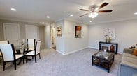 This single-floor residence offers a well-designed open-concept layout that seamlessly connects the living and dining areas, creating a comfortable and functional living environment. The living space is finished with plush, light gray carpeting that extends throughout, lending warmth underfoot and a cohesive aesthetic across the room.

Crown molding lines the perimeter of the ceilings, adding a refined architectural detail that elevates the overall finish of the space. Recessed lighting is strategically placed throughout the ceiling, supplemented by a ceiling fan with an integrated light fixture, ensuring both ample illumination and air circulation.

A standout feature is the pass-through window cut into the partial wall dividing the living area from the kitchen, offering a glimpse of warm wood cabinetry and providing convenient connectivity between the two spaces. The dining area accommodates a table and chairs, positioned near the entryway for easy access.

The light gray walls contribute to a bright, neutral palette that complements the natural and artificial lighting. A hallway leads further into the residence, hinting at additional rooms beyond the main living areas. Overall, the space presents a clean, move-in-ready aesthetic with practical design choices throughout.