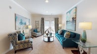 Located at 82 Ardmore Gardens Dr in Hardeeville, SC, this single-floor residence offers a thoughtfully designed layout with a cohesive coastal-inspired aesthetic throughout. The living area is bright and welcoming, finished with crown molding, recessed lighting, and plush carpet. A set of French doors with decorative drapery allows natural light to fill the space. The kitchen is well-appointed, featuring rich cherry wood cabinetry, granite countertops, a tile backsplash, and a full suite of stainless steel appliances including a range, microwave, dishwasher, and refrigerator. Wood-look flooring grounds the kitchen and adds warmth to the space. A peninsula with seating provides a natural transition into the adjacent dining area, which comfortably accommodates a round glass table with seating for four. The bedroom is generously sized, offering plush carpet, ample natural light through windowed walls with curtains, and space for a king-sized bed. The bathroom includes a tiled tub-shower combination, wood-look flooring, and a vanity with storage. Throughout the home, neutral wall tones are complemented by coordinated décor in teal and navy, creating a calm, polished ambiance.
