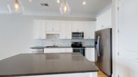 Located at 1414 Broadview Ave in Columbus, Ohio, this single-floor property offers a clean, contemporary design with thoughtful finishes throughout. The kitchen serves as a standout feature, showcasing white shaker-style cabinetry that extends to the ceiling, providing generous storage throughout. Dark quartz countertops offer a striking contrast against the bright cabinetry, while a marble-style subway tile backsplash adds a refined, textural detail to the space. A large central island with matching dark quartz surfaces provides additional prep space and serves as a natural gathering point. Stainless steel appliances — including a French door refrigerator, electric range with oven, built-in microwave, and dishwasher — complete the kitchen's modern, functional aesthetic. A single-basin undermount sink sits beneath a sleek faucet, complementing the overall design. Light hardwood flooring runs through the space, adding warmth to the otherwise cool-toned palette. A geometric glass pendant light fixture hangs above the island, contributing an elegant focal point. Crown molding adds a polished architectural detail, and recessed lighting ensures the space is well-lit throughout.