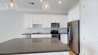 Located at 1414 Broadview Ave in Columbus, Ohio, this single-floor property offers a clean, contemporary design with thoughtful finishes throughout. The kitchen serves as a standout feature, showcasing white shaker-style cabinetry that extends to the ceiling, providing generous storage throughout. Dark quartz countertops offer a striking contrast against the bright cabinetry, while a marble-style subway tile backsplash adds a refined, textural detail to the space. A large central island with matching dark quartz surfaces provides additional prep space and serves as a natural gathering point. Stainless steel appliances — including a French door refrigerator, electric range with oven, built-in microwave, and dishwasher — complete the kitchen's modern, functional aesthetic. A single-basin undermount sink sits beneath a sleek faucet, complementing the overall design. Light hardwood flooring runs through the space, adding warmth to the otherwise cool-toned palette. A geometric glass pendant light fixture hangs above the island, contributing an elegant focal point. Crown molding adds a polished architectural detail, and recessed lighting ensures the space is well-lit throughout.