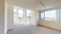 This single-floor residence is defined by an abundance of natural light and sweeping urban views, made possible by dramatic floor-to-ceiling windows that wrap the living area. The open layout connects the living space to a well-designed kitchen, which features dark espresso cabinetry, granite countertops, stainless steel appliances including a gas range and built-in microwave, and tile flooring. A peninsula with overhang seating separates the kitchen from the carpeted living area, creating a natural flow between spaces. Recessed lighting throughout the kitchen ensures a bright, functional environment even after dark.

The living room is particularly striking, with tall glass windows and rail-mounted track lighting that draw attention to the elevated city views. Soft carpeting and neutral walls create a calm, versatile backdrop. A second bedroom or bonus room features sliding glass door access to a private balcony, flooding the space with additional natural light.

Two bathrooms serve the residence. The primary bathroom is generously proportioned, offering a dual-sink vanity with granite countertops, dark cabinetry, a separate glass-enclosed shower, and a soaking tub. The secondary bathroom includes a combined tub and shower with tiled surround, a single-sink vanity, and matching cabinetry finishes, maintaining a cohesive aesthetic throughout.