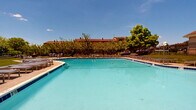 Located at 201 Idlewild Rd in Bel Air, Maryland, this outdoor pool facility serves as a central community amenity within a well-maintained residential complex. The pool itself is expansive, featuring clear turquoise water, dedicated lap lanes, and multiple entry points via stainless steel ladders. The pool deck is generously sized, offering ample space for circulation and relaxation around the perimeter.

The sun deck is outfitted with rows of modern sling-style chaise lounges arranged neatly along the poolside, providing residents with comfortable spaces to unwind and enjoy the open sky. A black iron perimeter fence encloses the entire pool area, ensuring both safety and a defined boundary between the pool grounds and the surrounding green space.

Well-maintained lawns extend beyond the fencing, lending a park-like quality to the environment. Mature trees provide natural shade and a pleasant visual backdrop throughout the space. A dedicated pool house structure with a distinctive cupola roofline is situated adjacent to the pool, likely serving as a support facility. The surrounding multi-story residential buildings are visible in the background, contextualizing the pool as a shared community resource. Under clear blue skies, the entire area projects a bright, welcoming, and resort-inspired atmosphere ideal for warm-weather recreation.