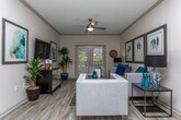 Located at 8064 S Fulton Pkwy in Fairburn, Georgia, this single-floor residence offers a thoughtfully designed open-concept layout that seamlessly connects the living, dining, and kitchen areas. The living room is a bright, inviting space featuring crown molding, a ceiling fan, and wood-look flooring, with large French doors that flood the room with natural light and provide access to an outdoor area. Framed artwork and contemporary furnishings contribute to the space's polished aesthetic.

The dedicated dining area accommodates a round table with ample seating and is accented by decorative wall art and a chair rail, adding architectural interest. The kitchen is outfitted with crisp white shaker-style cabinetry, light granite countertops, a neutral tile backsplash, and black appliances, creating a clean, functional workspace.

The primary bedroom is generously proportioned, featuring plush carpeting, a ceiling fan, multiple windows for natural light, and room for a substantial furniture arrangement. A secondary bedroom offers a comfortable, cozy atmosphere with carpeted flooring.

Two well-appointed bathrooms serve the residence — one featuring a tub/shower combination with wood-look flooring and white vanity cabinetry, and another with tile flooring, a large mirror, and a window for natural light. The overall palette throughout is soft and neutral, creating a cohesive and welcoming ambiance.