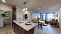 This well-designed single-floor residence offers a seamless open-concept layout connecting the kitchen, dining, and living areas into one cohesive and inviting space. The kitchen is a standout, featuring dark espresso cabinetry, granite countertops, a peninsula with an undermount sink and pendant lighting overhead, white subway tile backsplash, and a full suite of stainless steel appliances including a refrigerator with ice maker, electric range, and built-in microwave. Light wood-style flooring flows throughout the main living areas, enhancing the bright and airy ambiance. The living room is spacious and bathed in natural light through large windows with sheer drapery, creating a warm and welcoming atmosphere. The bedroom is a tranquil retreat, finished with plush carpet and floor-to-ceiling windows that invite abundant natural light. An en-suite bathroom features dark cabinetry, granite countertops, a walk-in glass shower, and built-in shelving. A second full bathroom offers a granite vanity, dark cabinetry, and a soaking tub with shower combination. Additional storage is thoughtfully incorporated throughout the space, including a walk-in closet visible from the kitchen area.