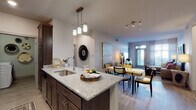 This well-designed single-floor residence offers a seamless open-concept layout connecting the kitchen, dining, and living areas into one cohesive and inviting space. The kitchen is a standout, featuring dark espresso cabinetry, granite countertops, a peninsula with an undermount sink and pendant lighting overhead, white subway tile backsplash, and a full suite of stainless steel appliances including a refrigerator with ice maker, electric range, and built-in microwave. Light wood-style flooring flows throughout the main living areas, enhancing the bright and airy ambiance. The living room is spacious and bathed in natural light through large windows with sheer drapery, creating a warm and welcoming atmosphere. The bedroom is a tranquil retreat, finished with plush carpet and floor-to-ceiling windows that invite abundant natural light. An en-suite bathroom features dark cabinetry, granite countertops, a walk-in glass shower, and built-in shelving. A second full bathroom offers a granite vanity, dark cabinetry, and a soaking tub with shower combination. Additional storage is thoughtfully incorporated throughout the space, including a walk-in closet visible from the kitchen area.