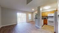 This single-floor residence offers a functional and cohesive layout with consistent design choices throughout. The open living area is bright and welcoming, featuring wood-look flooring, neutral gray walls, and a textured ceiling. Large vertical blinds cover a full sliding glass door that allows abundant natural light to fill the space, while an additional window further enhances the airy feel of the room.

The kitchen is semi-separated from the living area by a partial wall with a pass-through counter, creating a connected yet defined cooking space. It features warm honey-toned cabinetry, dark granite-style countertops, and white appliances including a refrigerator, range, and over-the-range microwave. Ample upper and lower cabinet storage is available throughout.

The bedroom offers a generously proportioned layout with vaulted ceilings, wood-look flooring, a window with outdoor views, and a bifold closet door providing organized storage. The bathroom includes a tub-shower combination with white tile surround, a toilet, and a vanity with matching warm wood cabinetry and dark countertops, all set on wood-look flooring. The overall ambiance is clean, neutral, and move-in ready.