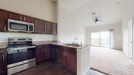 This single-floor residence is designed with an open-concept layout that seamlessly connects the kitchen and living area, creating a spacious and cohesive environment. The kitchen is a standout feature, outfitted with rich dark wood cabinetry, granite countertops, a subway tile backsplash, and a full suite of stainless steel appliances including a refrigerator, range, microwave, and dishwasher. A peninsula with a double sink offers additional workspace and naturally defines the transition into the living area. Throughout the main living spaces, soaring ceilings amplify the sense of openness, while ceiling fans provide comfort and airflow. The living area is finished with plush carpeting and is bathed in natural light, with a sliding glass door leading to a private balcony with open outdoor views. The bedroom continues the bright and airy feel, featuring large windows with blinds, soft carpet flooring, and elevated ceilings. The bathroom is well-appointed with dark wood vanity cabinetry, granite countertops, wood-look tile flooring, and a tiled bathtub surround, with direct access to a walk-in closet. Track lighting accents the main living space, adding a modern touch to this thoughtfully designed residence.