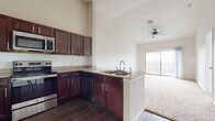This single-floor residence is designed with an open-concept layout that seamlessly connects the kitchen and living area, creating a spacious and cohesive environment. The kitchen is a standout feature, outfitted with rich dark wood cabinetry, granite countertops, a subway tile backsplash, and a full suite of stainless steel appliances including a refrigerator, range, microwave, and dishwasher. A peninsula with a double sink offers additional workspace and naturally defines the transition into the living area. Throughout the main living spaces, soaring ceilings amplify the sense of openness, while ceiling fans provide comfort and airflow. The living area is finished with plush carpeting and is bathed in natural light, with a sliding glass door leading to a private balcony with open outdoor views. The bedroom continues the bright and airy feel, featuring large windows with blinds, soft carpet flooring, and elevated ceilings. The bathroom is well-appointed with dark wood vanity cabinetry, granite countertops, wood-look tile flooring, and a tiled bathtub surround, with direct access to a walk-in closet. Track lighting accents the main living space, adding a modern touch to this thoughtfully designed residence.