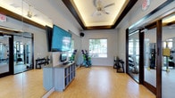The Fitness On Demand Studio is a thoughtfully designed single-floor workout space built to support a wide range of exercise routines and on-demand fitness programming. The studio's most striking architectural feature is its coffered tray ceiling, accented with warm recessed lighting and dark wood trim, which adds a polished, refined aesthetic to the space. A contemporary ceiling fan keeps the environment comfortable during active sessions.

The room is anchored by a large wall-mounted flat-screen display paired with an interactive Fitness On Demand console, enabling users to access a full library of virtual instructor-led classes. A built-in storage credenza with open cubbies provides convenient organization for accessories and personal items. Full-length mirrors line one wall, enhancing the sense of openness and allowing users to monitor their form.

The studio is well-equipped with a variety of free weights, kettlebells, resistance tools, and exercise bars neatly arranged on dedicated racks and stands. Cork flooring throughout the space offers both durability and a cushioned, joint-friendly surface ideal for floor exercises and movement-based workouts. Natural light flows in through a window with a pleasant outdoor view, contributing to an energizing and welcoming atmosphere. The space is compact yet functional, making it well-suited for individual or small group training sessions.