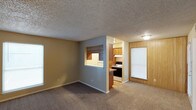 This single-story residence in Sherman offers a practical and functional layout with distinct living, sleeping, and kitchen areas. The living room is spacious and carpeted, featuring neutral-toned walls, a textured ceiling, and a window that allows natural light to fill the space. A partial dividing wall with a pass-through opening connects the living area to the kitchen, creating an open feel while maintaining separation between spaces. An entry area adjacent to the living room features warm wood-panel accent walls, adding a touch of character.

The kitchen is equipped with wood-toned cabinetry, a laminate countertop with a stainless steel sink, hardwood-style flooring, and white appliances including a refrigerator and an electric range. Flush-mounted ceiling lights provide ample illumination throughout the kitchen.

The bedrooms are carpeted and offer neutral walls with textured ceilings. One bedroom includes a ceiling fan with light fixture, while another features a large window for natural light and a third provides a sliding glass door leading to an outdoor area, along with an open closet with a hanging rod.

The bathroom includes a tub and shower combination with a white surround panel enclosure and built-in recessed shelving niches, offering a clean and functional design.