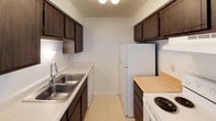 This single-floor unit is designed with a practical and straightforward layout. The galley-style kitchen is efficiently organized, featuring dark espresso cabinetry both above and below the countertops, a double stainless steel sink, white appliances including a coil-burner range and refrigerator, and light-toned countertops. Tile flooring and a ceiling light fixture complete the functional space.

The living area is generously sized, finished with wall-to-wall neutral carpet and a textured ceiling. A ceiling fan provides air circulation, and a sliding glass door floods the room with natural light while offering views of the surrounding outdoor area. The open flow between the living and dining areas, visible through a pass-through to the kitchen, adds to the sense of connected space.

Multiple bedrooms are carpeted and feature textured ceilings, neutral walls, and windows fitted with horizontal blinds that allow natural light. The rooms offer a clean, versatile canvas suitable for various furniture arrangements.

The bathrooms include a full bath with a white tub and shower combination, white tile surround, vanity with sink, and toilet. An additional bathroom provides a toilet and window with privacy blinds. Overall, the unit presents a clean, functional, and move-in ready environment.