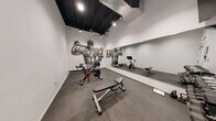 Located at 1300 S Casino Center Blvd in Las Vegas, this dedicated exercise room delivers a focused and energetic fitness environment within a compact single-floor footprint. The space is defined by clean white walls that serve as the backdrop for a striking, large-scale mural depicting a Las Vegas Raiders athlete — a bold artistic centerpiece that infuses the room with local sports culture and motivational energy.

The flooring consists of durable gray tiles, providing a practical and polished surface suited for a range of workout activities. A full-length wall mirror runs along one side of the room, visually expanding the space and supporting form-conscious training. Recessed lighting and exposed black ceiling elements above create an industrial-modern aesthetic that keeps the atmosphere dynamic without feeling cluttered.

Equipment is thoughtfully arranged and includes multiple Peloton-style stationary bikes, a multi-tier dumbbell rack with a varied weight selection, kettlebells, an adjustable weight bench, and a wall-mounted flat-screen television. Exposed ductwork on the ceiling reinforces the industrial character of the space.

A frosted-glass entry door, exit signage, and a slim stainless steel waste receptacle contribute to a clean, professional finish. Despite its intimate scale, this exercise room is efficiently outfitted to support cardio, strength, and cross-training workouts.