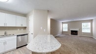Located at 1300 Beaver Ruin Rd in Norcross, Georgia, this single-floor residence offers a well-designed layout that balances comfort and functionality. The kitchen is a standout feature, equipped with stainless steel appliances including a refrigerator, range, microwave, and dishwasher, all complemented by crisp white cabinetry and a granite-topped peninsula that provides additional prep and dining space. Light wood-style flooring runs throughout the kitchen, adding warmth and easy maintenance underfoot. The open flow leads into a generously sized living area, where plush carpeting, a classic wood-burning fireplace with a white mantel, and multiple windows create a bright and inviting atmosphere. The bedrooms are carpeted and well-proportioned, with at least one room featuring a ceiling fan with light fixture and a window for natural light. A hallway connects the sleeping areas to a full bathroom, which includes a tub/shower combination, granite vanity countertop, and wood-style flooring. A dedicated laundry area with side-by-side washer and dryer hookups adds everyday convenience. Throughout the unit, neutral beige tones, textured ceilings, and clean white trim provide a cohesive, move-in-ready aesthetic.