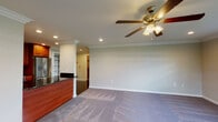 This single-floor residence at Fairfield Knolls at Sayville offers a thoughtfully designed open layout with consistent, quality finishes throughout. Crown molding runs through each room, adding a refined architectural detail that ties the spaces together cohesively.

The living area is generously proportioned, featuring plush carpeting, recessed lighting, and a ceiling fan with light fixture. It flows seamlessly toward the kitchen, which is separated by a decorative column and peninsula with a dark granite countertop. The kitchen is well-equipped with rich cherry wood cabinetry, dark tile flooring, black granite countertops, and a full suite of stainless steel appliances, including a French door refrigerator, built-in microwave, and dishwasher.

The bedrooms are spacious and carpet-lined, each equipped with ceiling fans and recessed lighting. One bedroom features a walk-in closet with built-in shelving and organizers, while multiple rooms benefit from large windows that invite abundant natural light and outdoor views. A hallway with tile flooring connects the rooms efficiently.

The bathroom is elegantly finished, showcasing a large glass-enclosed shower with neutral tile surround, a decorative mosaic accent border, and a cherry wood vanity topped with dark granite. Overall, the space presents a clean, functional, and polished living environment.