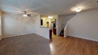 This two-story residence offers three bedrooms and two and a half bathrooms across a well-organized floor plan. The main level features an open living area with warm hardwood-style flooring that flows into the kitchen, which is equipped with rich dark cabinetry, granite-style countertops, a stainless steel refrigerator, and a peninsula that separates it from the living space. A ceiling fan with light fixture keeps the living area comfortable, and a front entry door with a adjacent window allows natural light into the space. A half bathroom on the main level includes a dark wood vanity with a granite-style countertop and hardwood-style flooring, providing convenient guest access. A staircase leads to the upper level, where all three bedrooms are located. Each bedroom features plush carpet, ceiling fans, and windows with blinds for natural light and privacy. The bedrooms are served by two full bathrooms, each featuring a tub-shower combination with tile surround, dark wood vanity, granite-style countertop, and hardwood-style flooring. Multiple walk-in closets with built-in shelving and hanging rods provide ample storage throughout the upper level. The overall aesthetic is neutral and inviting, with warm tones carried consistently across both floors.