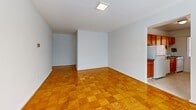 Located at 825 New Hampshire Ave NW in Washington, DC, this 2-bedroom, 1-bathroom unit offers a practical and well-laid-out single-floor plan. Polished parquet wood flooring flows consistently throughout the living areas and both bedrooms, lending warmth and a classic character to the space. The open living area is bright and versatile, with flush ceiling lighting and a seamless connection to the kitchen. The kitchen features warm honey-toned wood cabinetry, a gas range, a stainless steel sink with granite-style countertops, and a window that fills the space with natural light. Both bedrooms are comfortably sized, with the primary bedroom offering generous proportions, large windows with views of surrounding greenery, and a wall-mounted heating unit. The second bedroom similarly benefits from a wide window that invites natural light. A hallway connects the main living areas to the bathroom, which is finished in clean white tile with a full bathtub-shower combination and a single vanity. The unit's consistent white walls and gleaming floors create a bright, cohesive ambiance throughout.