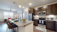 This single-floor residence offers a thoughtfully designed open-concept layout that seamlessly connects the kitchen, dining, and living areas. The kitchen is a standout feature, showcasing rich dark espresso cabinetry, granite countertops, a classic subway tile backsplash with under-cabinet lighting, and a full suite of stainless steel appliances including a refrigerator, electric range, and built-in microwave. A granite-topped island with bar seating serves as both a functional workspace and a casual dining spot, accented by stylish pendant lighting overhead. The living area is bright and welcoming, with large windows fitted with blinds that invite natural light and offer views of the surrounding neighborhood. Wood-style flooring runs throughout the main living spaces, adding warmth and continuity. The bedrooms are carpeted and comfortably sized, each with windows that provide natural light. The bathroom is well-finished with tile-surround tub and shower, wood-look flooring, and a granite-topped vanity with dark cabinetry that mirrors the kitchen aesthetic. A spacious walk-in closet with built-in shelving and hanging rods provides generous storage. Overall, the space presents a clean, modern aesthetic with consistent finishes and a functional, comfortable layout.