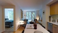 This thoughtfully designed single-floor residence offers a seamless blend of comfort and contemporary style. The open-plan layout connects the dining and living areas, creating a cohesive and inviting atmosphere throughout. Light hardwood flooring runs underfoot, lending warmth to the space, while crisp white walls and ceilings provide a clean, airy backdrop that enhances the sense of openness.

The living area is anchored by a plush sofa adorned with textured cushions, paired with a low-profile coffee table and complementary accent chairs. Artistic touches — including a woven macramé wall hanging and a sculptural wall clock — add personality and visual interest. Curated décor such as dried botanicals, ceramic vessels, and layered lighting create a warm, inviting ambiance.

Large floor-to-ceiling windows and a glass door flood the space with natural light and frame picturesque views of lush, mature greenery beyond. The dining area features a sleek white table with contemporary seating, positioned to benefit from both natural light and the flow of the living space.

The overall ambiance is modern yet cozy, with thoughtful styling that balances aesthetic appeal and everyday livability, making this a welcoming and well-appointed home.