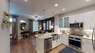 This single-floor residence is designed with an open-concept layout that seamlessly connects the kitchen and living area. The kitchen is a standout feature, equipped with stainless steel appliances including a gas range, microwave, refrigerator, and dishwasher. White shaker-style cabinetry with frosted glass uppers pairs with striking granite countertops, while a large central island with a farmhouse sink and pendant lighting serves as both a functional workspace and a social hub. A decorative arabesque tile backsplash adds a refined touch, and warm hardwood flooring flows throughout the main living areas.

The living space transitions naturally from the kitchen and is brightened by natural light through slatted blinds and patterned curtains. Both bedrooms feature plush carpet, ceiling fans, and generous windows. The primary bedroom is distinguished by a bold teal accent wall adorned with circular wall art, lending a sophisticated and artistic character to the space.

The bathroom offers a long, functional layout with dual under-mount sinks set into dark granite countertops, white cabinetry with brushed nickel hardware, and a tub-shower combination. Recessed and sconce lighting provide ample illumination throughout this well-appointed residence.