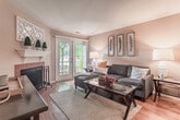 Located at 3700 Steeplechase Dr in Williamsburg, Virginia, this single-floor residence offers a well-designed layout with a warm, inviting ambiance throughout. The living room serves as a central gathering space, highlighted by a tile-surround fireplace with a decorative white mantel and French doors that open to an outdoor area, flooding the room with natural light. Rich hardwood flooring flows through the living area and kitchen, adding warmth and continuity.

The kitchen features a pass-through peninsula design with warm wood cabinetry, dark countertops, and black appliances, creating a functional and connected cooking space that opens toward the main living area. Multiple bedrooms are finished with plush carpeting and offer generous natural light through large windows with blinds and curtains. At least one bedroom includes a spacious walk-in closet with built-in shelving, providing ample storage.

The bathrooms are appointed with wood-toned vanity cabinetry, hardwood flooring, and tiled tub-shower combinations. The neutral color palette of warm beige and soft grey tones carried throughout the residence creates a cohesive and comfortable atmosphere. The overall layout, as visible in the dollhouse view, is thoughtfully organized to maximize both privacy and open living space.