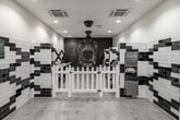 Located at 401 N Main St in Santa Ana, California, this purpose-built pet grooming space is thoughtfully designed with both functionality and visual flair in mind. The single-floor layout is anchored by a dramatic floor-to-ceiling photographic mural of a dog's face, serving as an eye-catching focal point at the far end of the room.

The interior is defined by bold black-and-white subway tile work arranged in geometric, diamond-patterned designs that line the walls throughout. The tiling not only adds a striking aesthetic but also ensures surfaces are durable and easy to maintain — ideal for a grooming environment. Polished concrete floors complement the monochromatic palette while providing practicality underfoot.

The grooming area features dedicated stations equipped with adjustable grooming tables and mounted hose attachments, as well as a stainless steel wash station for bathing pets. White picket-style dividers separate the individual grooming bays, adding a charming detail to the otherwise modern design.

Recessed ceiling lighting and flush-mounted HVAC units ensure the space is well-lit and climate-controlled. Near the entrance, a welcoming waiting area features lush potted plants, a simple bench, and decorative accents, creating a calm and inviting atmosphere for both pets and their owners. The overall design balances professional utility with a polished, distinctive aesthetic.