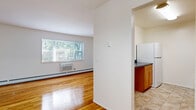 Located at 21 Vermeer Dr in South Amboy, NJ, this one-bedroom, one-bathroom residence offers a practical and well-organized floor plan. Entry is gained via a staircase with classic wood-tread steps, white risers, and a dark wood handrail, leading up to the main living level. The open-concept living and dining area is a highlight of the space, featuring gleaming hardwood floors that run throughout, crisp white walls, and a large window that fills the room with natural light and views of greenery outside. A wall pass-through connects the living area to the kitchen, enhancing the sense of openness. The galley-style kitchen is efficiently designed with warm honey-toned wood cabinetry, dark countertops, a white tile backsplash, and white appliances including a refrigerator, range, microwave, and dishwasher. Tile flooring completes the kitchen's clean, functional aesthetic. The spacious bedroom continues the hardwood flooring and features a wide window with outdoor views and a wall-unit air conditioner. Two closets provide ample storage. The full bathroom is finished with neutral beige tile on the floors and shower surround, complemented by a white vanity with a mirrored medicine cabinet and a full tub-shower combination.