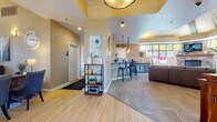 This single-floor community clubhouse is thoughtfully designed to offer a warm and functional gathering space. The open layout flows seamlessly from the entry area through the main lounge and into supporting spaces, creating an inviting and well-connected environment throughout.

The entry area features light wood-look flooring, a decorative pendant light with a distinctive tray ceiling accent in yellow, and an open shelving unit that adds a welcoming touch. Adjacent to the entry is a private office area highlighted by large windows that overlook an outdoor courtyard, filling the space with natural light. A substantial wood desk paired with upholstered chairs makes this area both professional and comfortable.

The kitchenette is outfitted with white upper cabinetry, a subway tile backsplash, sleek quartz countertops, and a raised bar with industrial-style metal stools. Warm Edison-style pendant lights hang above, lending the area a relaxed yet refined atmosphere.

The main lounge area is a standout feature, showcasing a floor-to-ceiling stacked stone fireplace flanked by large multi-pane windows that bring in abundant natural light and views of mature trees outside. Tray ceilings with bold yellow accents add architectural interest overhead, while plush carpeting and comfortable seating arrangements create a cozy, community-centered retreat.