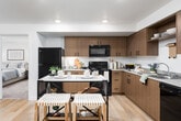 This single-floor residence offers a thoughtfully designed open-concept layout that seamlessly connects the kitchen, dining, and living areas. The kitchen is a standout feature, showcasing warm wood cabinetry, light countertops, and a full suite of black appliances including a refrigerator, range, microwave, and dishwasher. Light hardwood-style flooring runs throughout the main living areas, adding a clean, cohesive look. The living room benefits from natural light through large vertical-blind windows and sliding doors that open to a balcony with outdoor views. The space accommodates multiple bedrooms, each carpeted for comfort and fitted with generous windows that invite natural light. The primary bedroom includes large windows with exterior views and ample room for furnishings. Additional bedrooms are well-proportioned with versatile layouts suitable for various needs. The bathrooms feature wood-toned vanities with neutral countertops and hardwood-style flooring, with one bath offering a shower-tub combination. Throughout the residence, a neutral color palette of whites and warm wood tones creates a bright, welcoming ambiance. Recessed and flush-mount lighting ensures consistent illumination across all rooms, complementing the natural light found throughout this functional and modern living space.