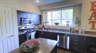 This thoughtfully designed 3-floor residence offers a functional and stylish living experience across multiple levels. The kitchen stands out as a centerpiece of the home, showcasing rich dark cabinetry that contrasts beautifully with granite-style countertops. Stainless steel appliances — including a range, microwave, and dishwasher — lend a contemporary, polished feel to the space. A large double-basin sink sits beneath a generous picture window that frames lush, tree-lined views and floods the kitchen with natural light, creating an inviting atmosphere for cooking and entertaining. A kitchen island provides additional prep and dining space, enhancing the room's practicality. The warm-toned walls complement the dark wood finishes throughout, striking a balance between modern design and cozy comfort. Hardwood-style flooring ties the space together with a clean, durable aesthetic. With three full floors, this home provides ample room for living, working, and relaxing, offering versatile spaces suited to a variety of lifestyles. The abundant natural light and thoughtful design details evident in the kitchen suggest a consistent level of quality and care carried throughout the entire residence.