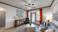 This thoughtfully designed one-bedroom, one-bathroom unit in Humble, TX offers a cohesive and modern interior across a single floor. The living room is a welcoming space highlighted by crown molding, wood-look flooring, a ceiling fan with lighting, and large windows dressed with bold accent curtains that invite abundant natural light. The open layout flows naturally into the kitchen, which features rich dark cabinetry, granite-style countertops, stainless steel appliances including a refrigerator, range, and microwave, and wood-look flooring that ties the common areas together seamlessly. The bedroom is a comfortable retreat finished with plush carpet, a ceiling fan, and generously sized windows offering outdoor views. A dedicated closet provides practical storage. The bathroom is clean and well-finished, with a granite-topped vanity, dark cabinetry, wood-look flooring, and a full tub-shower combination with tile surround. A hallway connects the private and shared areas of the unit efficiently. Throughout the space, consistent design choices — including matching cabinetry tones, neutral walls, and coordinated fixtures — create a polished and functional living environment.