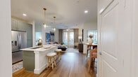 Located at 7051 Stacy Rd in McKinney, TX, this well-appointed 2-bedroom, 3-bathroom residence offers a thoughtfully designed single-floor layout with modern finishes throughout. The open-concept kitchen is a standout feature, boasting sage-green cabinetry with gold hardware, a white quartz island with an undermount sink, stainless steel appliances, a subway tile backsplash, and elegant pendant lighting — all set over durable wood-look flooring. The kitchen flows seamlessly into the living room, which features a ceiling fan, French doors that invite natural light, and access to a private balcony. The primary bedroom offers a comfortable, carpeted retreat with large windows, while its en-suite bathroom features dual vanities with sage cabinetry, gold fixtures, wood-look flooring, and direct access to a well-organized walk-in closet with built-in shelving and hanging rods. The second bedroom is equally bright, with large windows and plush carpet. A second walk-in closet offers additional storage with open shelving. Bathrooms feature neutral tile surrounds and a tub-shower combination with gold fixtures. The overall ambiance is clean, contemporary, and cohesive throughout.