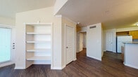 This single-story residence offers a well-organized layout with a variety of functional spaces finished in warm, neutral tones throughout. The main living area features vaulted ceilings with a ceiling fan and light fixture, large windows fitted with horizontal blinds, and dark hardwood-style flooring that extends through much of the unit, creating a cohesive, polished look.

The kitchen is equipped with warm oak cabinetry offering generous storage, granite-style countertops, a double-basin stainless steel sink, and white appliances including an electric range, over-the-range microwave, and dishwasher. A hallway connects the main areas and includes built-in open shelving ideal for organization or display, alongside white panel doors with crown molding accents.

The bedrooms are carpeted and generously sized, each featuring ceiling fans, natural light from windows with blinds, and ample wall space. A dedicated dining or flex room displays crown molding detailing and hardwood-style flooring with a pass-through window view toward the entryway.

The bathroom includes a wood-toned vanity with a single sink, a large mirror, recessed lighting, and hardwood-style flooring. A louvered utility closet houses the water heater nearby, keeping practical elements neatly contained within the overall floor plan.