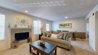 This single-floor residence offers a thoughtfully designed open-concept layout that seamlessly connects the living, dining, and kitchen areas. The living room is a welcoming focal point, centered around a stone-surround fireplace flanked by large windows with plantation shutters that allow generous natural light to fill the carpeted space. Recessed lighting overhead adds warmth throughout. The dining area flows directly from the living room, creating an ideal setting for everyday living and entertaining. The kitchen is efficiently laid out in a U-shape, featuring warm oak cabinetry, dark granite-style countertops, a breakfast bar pass-through, and white appliances including a range, microwave, and sink — all set on easy-care hardwood-style flooring. Two bedrooms provide comfortable accommodations; the primary bedroom includes a walk-in closet, while the second bedroom opens conveniently toward the main living area. The bathroom is well-appointed with warm wood cabinetry, a large vanity mirror, and hardwood-style flooring. A standout practical feature is the in-unit laundry area located just off the bathroom. Throughout, the space maintains a cohesive, neutral palette with warm accents, creating a comfortable and inviting atmosphere.