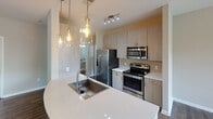 Located at 12024 Landing Place Ln in Charlotte, NC, this single-floor residence offers a thoughtfully designed layout with modern finishes throughout. The kitchen is a standout feature, showcasing light wood cabinetry, quartz countertops, stainless steel appliances including a refrigerator, range, and microwave, and a large island with an undermount sink. Stylish Edison-bulb pendant lights hang above the island, adding a warm, contemporary ambiance. The open dining area flows naturally from the kitchen, featuring durable hardwood-style flooring, track lighting, and a window that fills the space with natural light. The living area continues the same flooring and offers a generous, open feel with a ceiling fan and access to multiple doorways. The bedroom is finished with plush carpeting, neutral walls, a ceiling fan, and a window overlooking the surrounding neighborhood, providing a calm and comfortable retreat. The bathroom is well-equipped with wood-style flooring, a granite-topped vanity with an undermount sink, a glass-enclosed walk-in shower with decorative tile accents, and clean, modern fixtures throughout. Neutral tones and consistent finishes create a cohesive and inviting atmosphere across the entire unit.