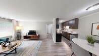 Located at 420 Kellogg St in Ann Arbor, Michigan, this efficiently designed single-floor space offers a well-organized layout comprising a living room, kitchen, two office rooms, a bathroom, and a hallway. The living room is bright and inviting, featuring hardwood-style flooring, crown molding, and a large window that fills the space with natural light and offers views of the surrounding greenery. The kitchen is thoughtfully laid out in a galley style, equipped with dark wood cabinetry, white countertops, stainless steel appliances, and wood-look flooring — maximizing both storage and functionality. Two dedicated office rooms provide flexible workspace; one features an L-shaped desk, carpet flooring, and a wide window overlooking the outdoors, while the second includes a lateral filing cabinet, seating area, and a corkboard wall display, both benefiting from natural light. The bathroom is clean and well-appointed, featuring a dark wood vanity with a white countertop, a shower-tub combination with a patterned curtain, wood-look flooring, and neutral wall tones. Throughout the space, a consistent palette of soft grays, warm neutrals, and natural wood tones creates a cohesive and professional ambiance.