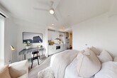 Located at 312 W Republican Street in Seattle's desirable Queen Anne neighborhood, this efficiently designed studio unit makes excellent use of its single-floor layout. The open-plan main area seamlessly integrates the sleeping, living, and kitchen spaces into one cohesive environment, finished with light wood-style flooring and crisp white walls that enhance the sense of openness.

The kitchenette is tucked neatly along one wall, featuring white cabinetry with open shelving, a stainless steel refrigerator, a microwave, a single-basin sink, and recessed lighting overhead. A ceiling fan with integrated lighting keeps the space comfortable year-round. A dedicated workspace with room for a desk sits adjacent to the kitchen area, making the unit well-suited for remote work.

A large picture window floods the living area with natural light and frames impressive elevated views of the Seattle skyline and Elliott Bay waterfront beyond. The bathroom is clean and modern, appointed with a white quartz vanity, under-mount sink, brushed nickel hardware, and a full mirror. A separate closet with a clothing rod and additional storage provides practical organization. Sliding doors and light-toned finishes throughout maintain a cohesive, contemporary aesthetic ideal for urban living.